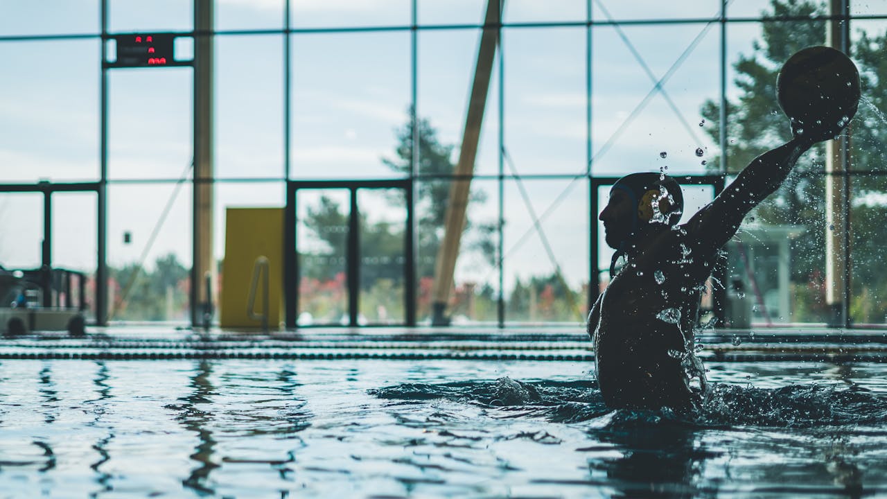 Crafting Captivating Headlines: Your awesome post title goes here Silhouette of a water polo player mid-action with water splashes inside an indoor pool.