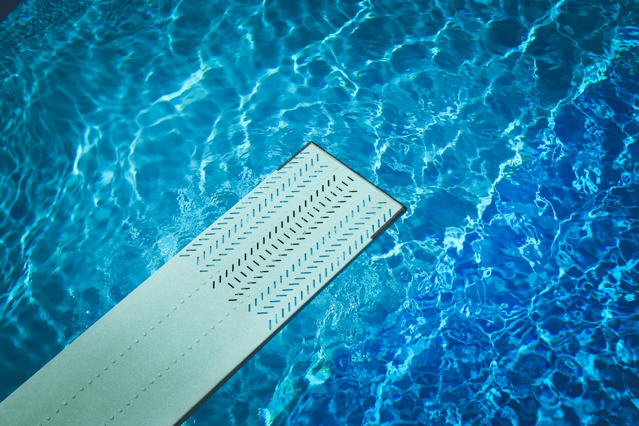 The Art of Drawing Readers In: Your attractive post title goes here A diving board over a sunlit swimming pool, reflecting vibrant blue water patterns.